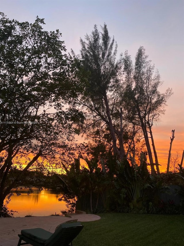 yard at dusk featuring a patio and a water view