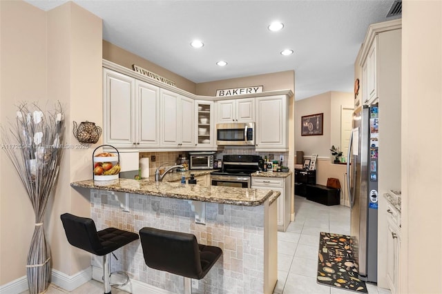 kitchen featuring white cabinetry, light stone counters, light tile patterned floors, kitchen peninsula, and appliances with stainless steel finishes