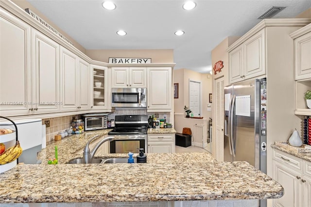 kitchen featuring kitchen peninsula, light stone countertops, backsplash, appliances with stainless steel finishes, and sink