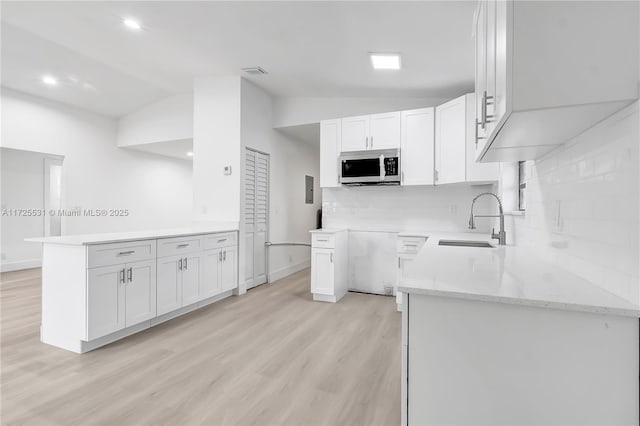 kitchen with kitchen peninsula, vaulted ceiling, backsplash, white cabinets, and sink