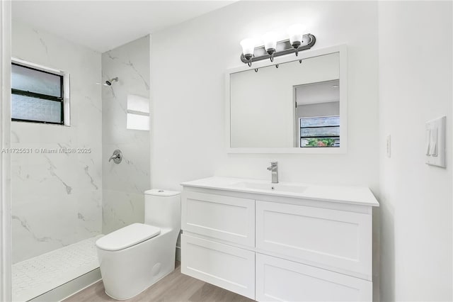 bathroom featuring toilet, vanity, tiled shower, and hardwood / wood-style floors