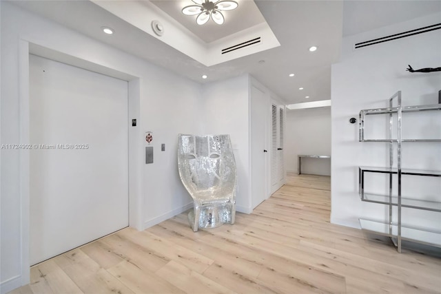 corridor with a raised ceiling and light hardwood / wood-style flooring