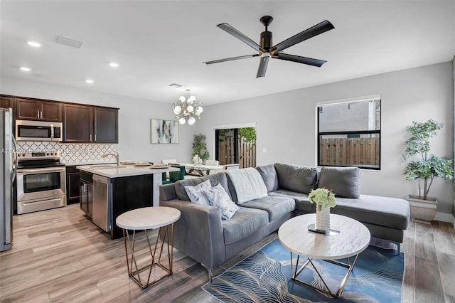 living room featuring light hardwood / wood-style floors, sink, and ceiling fan with notable chandelier