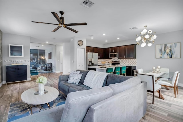 living room featuring ceiling fan with notable chandelier and light wood-type flooring