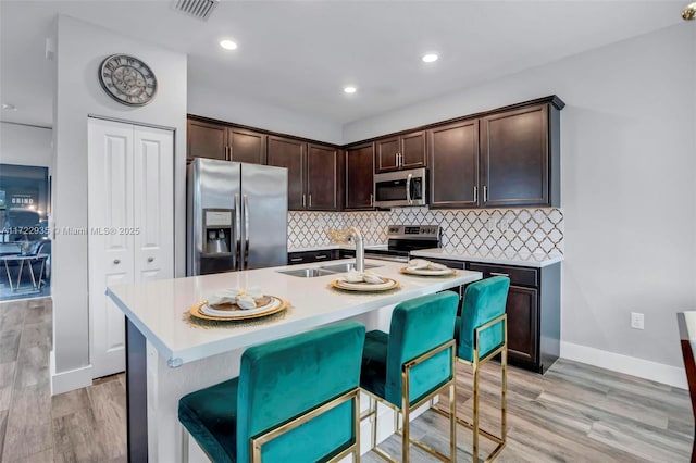 kitchen featuring dark brown cabinetry, stainless steel appliances, an island with sink, sink, and a breakfast bar