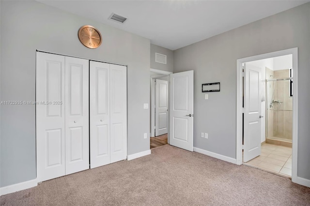 unfurnished bedroom with a closet, light colored carpet, and ensuite bath