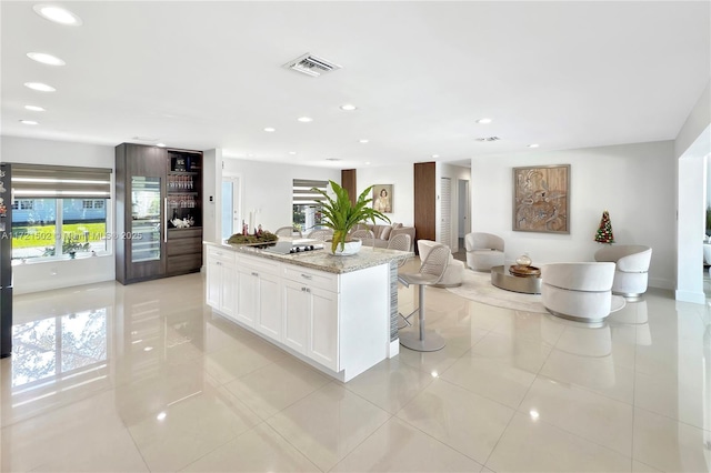 kitchen with a kitchen island, white cabinets, light tile patterned floors, and light stone countertops