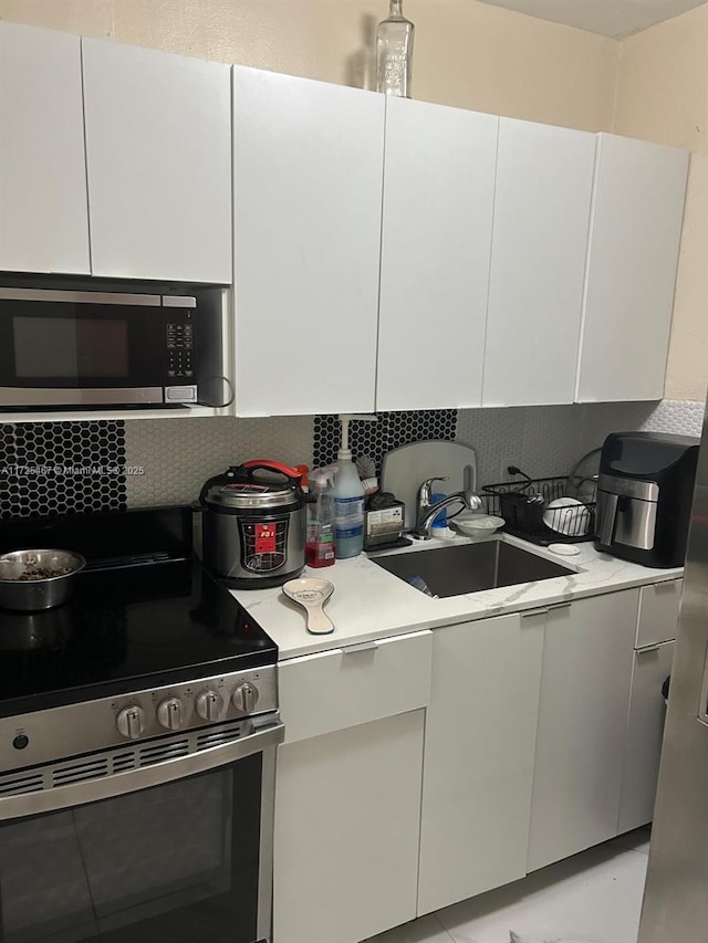 kitchen featuring stainless steel appliances, white cabinetry, decorative backsplash, and sink