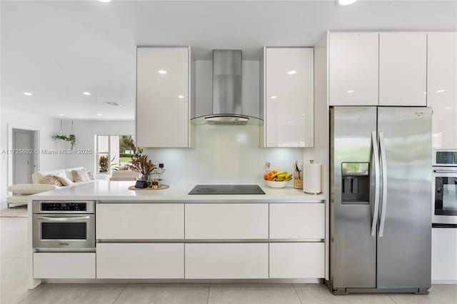 kitchen featuring light tile patterned floors, stainless steel appliances, wall chimney exhaust hood, and white cabinetry