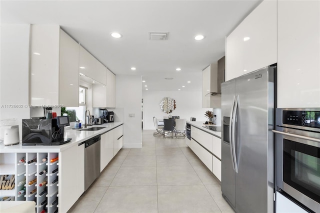 kitchen featuring white cabinets, wall chimney exhaust hood, stainless steel appliances, sink, and light tile patterned floors