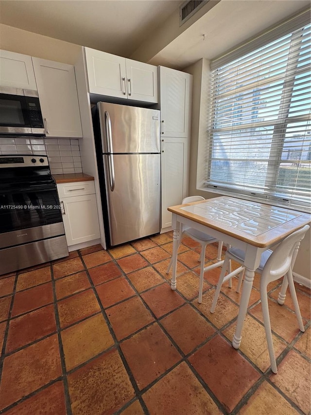 kitchen with stainless steel appliances, white cabinets, tile patterned flooring, and backsplash