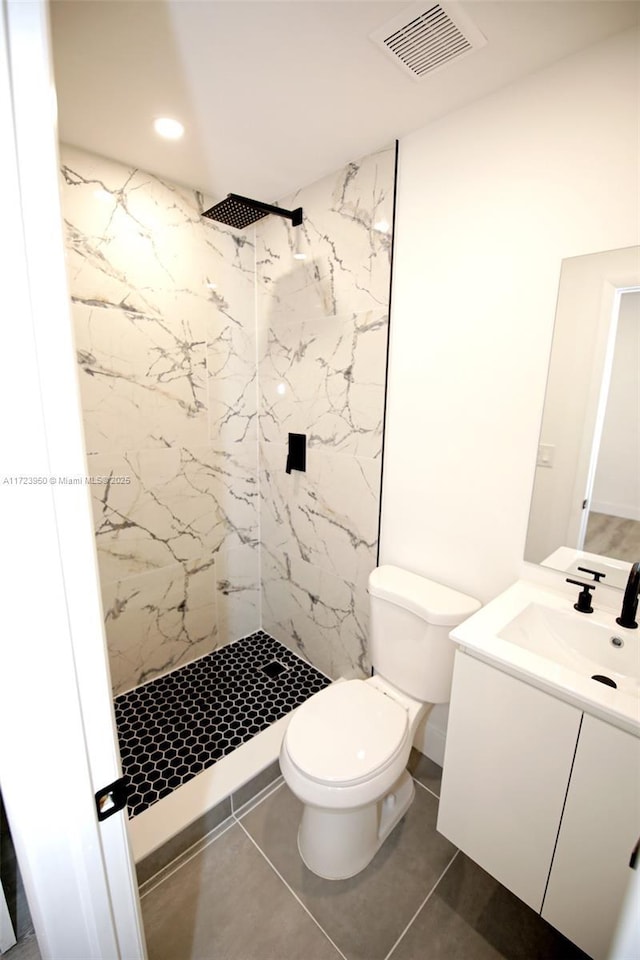 bathroom featuring tile patterned flooring, a tile shower, vanity, and toilet