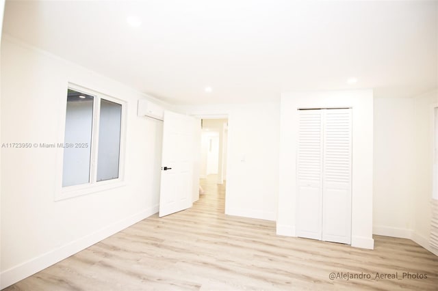 unfurnished bedroom featuring a wall unit AC, a closet, and light hardwood / wood-style flooring