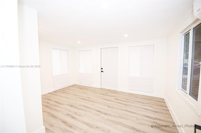 unfurnished room with a wall unit AC and light hardwood / wood-style floors