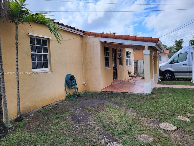 exterior space with a patio area, a yard, a tiled roof, and stucco siding