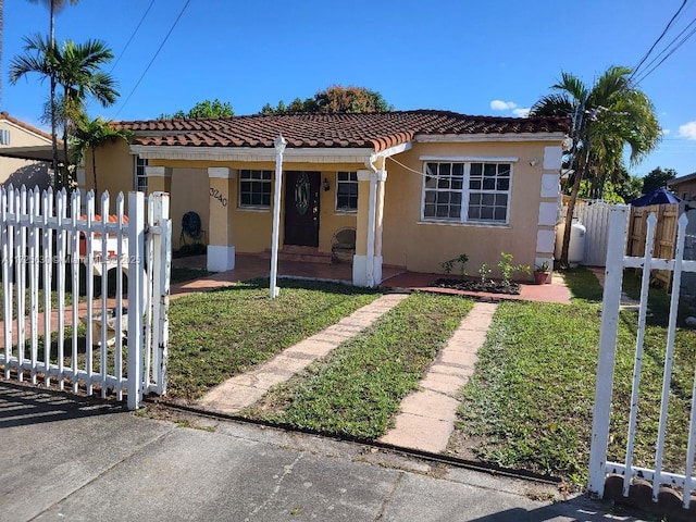 bungalow featuring fence, a tiled roof, a gate, stucco siding, and a front lawn