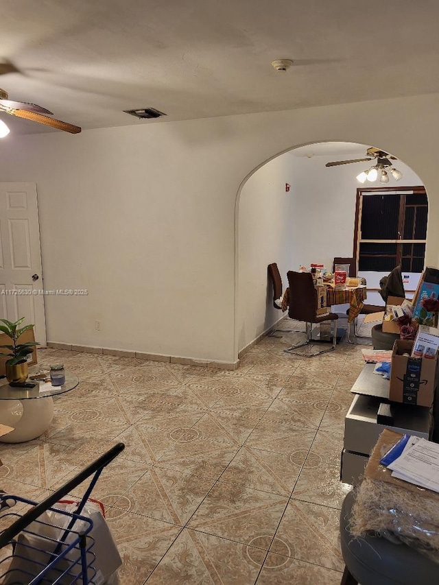 living area featuring arched walkways, light tile patterned flooring, visible vents, and a ceiling fan