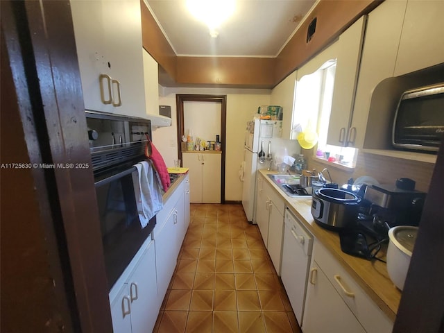 kitchen with light tile patterned floors, white appliances, a sink, white cabinets, and light countertops