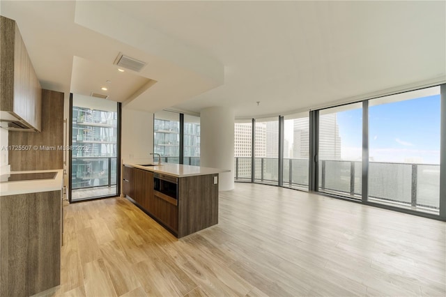 kitchen featuring a center island with sink, light hardwood / wood-style floors, a wall of windows, black electric stovetop, and sink