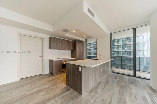 kitchen featuring light hardwood / wood-style flooring, a kitchen island with sink, a wall of windows, a breakfast bar area, and sink