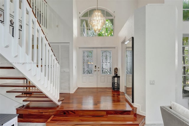 foyer entrance with a towering ceiling, french doors, wood-type flooring, and a chandelier