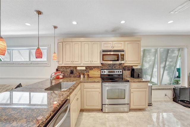 kitchen with decorative light fixtures, appliances with stainless steel finishes, cream cabinetry, and sink