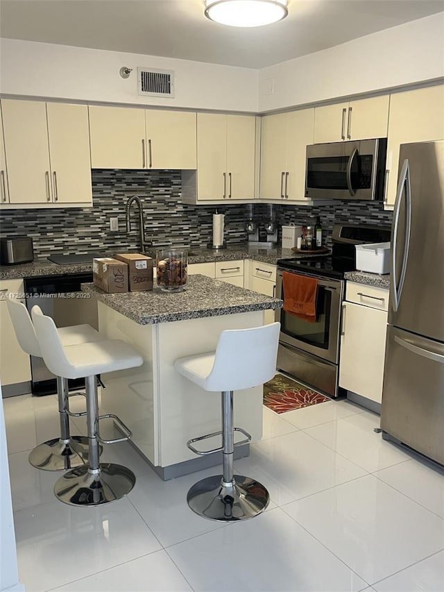 kitchen featuring stainless steel appliances, cream cabinets, decorative backsplash, and a kitchen bar