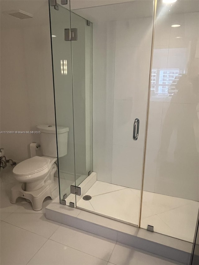 bathroom featuring toilet, a shower with shower door, and tile patterned floors