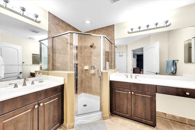 bathroom featuring tile patterned flooring, a textured ceiling, walk in shower, and vanity