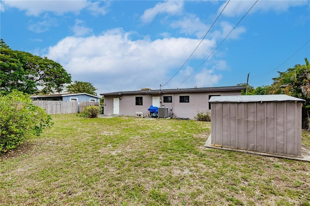 back of house with central air condition unit, a storage unit, and a yard