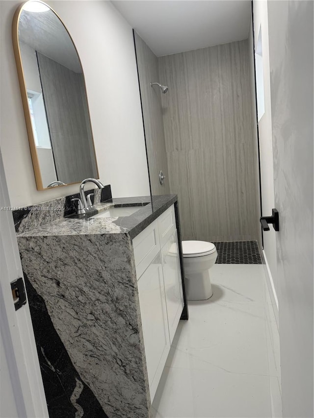 bathroom with toilet, a tile shower, and vanity