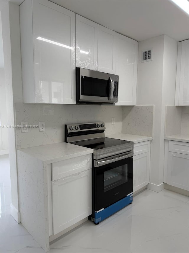 kitchen with appliances with stainless steel finishes, tasteful backsplash, and white cabinetry