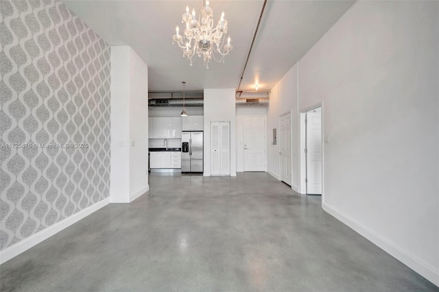 unfurnished living room featuring sink, a notable chandelier, and concrete flooring