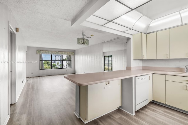 kitchen with light hardwood / wood-style floors, kitchen peninsula, white dishwasher, sink, and an inviting chandelier