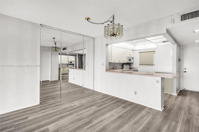 kitchen with white cabinets, a textured ceiling, white appliances, kitchen peninsula, and a chandelier