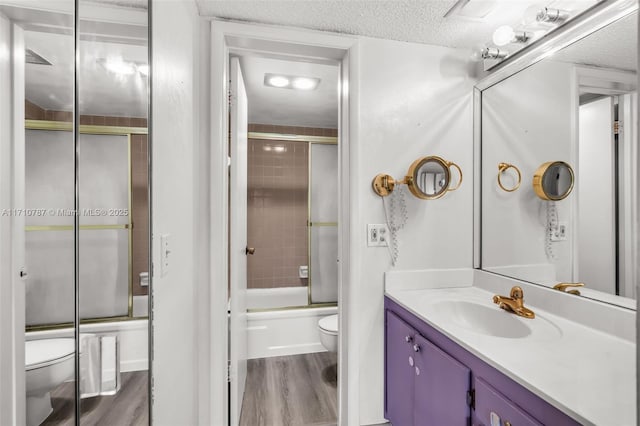 full bathroom with toilet, hardwood / wood-style flooring, a textured ceiling, shower / bath combination with glass door, and vanity