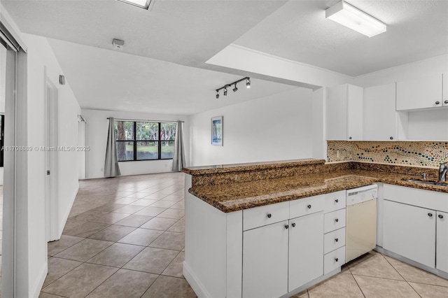 kitchen featuring dishwasher, kitchen peninsula, dark stone counters, white cabinets, and backsplash