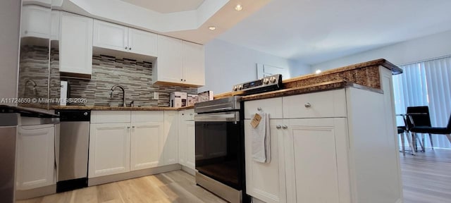 kitchen with light wood-type flooring, backsplash, white cabinetry, appliances with stainless steel finishes, and dark stone countertops