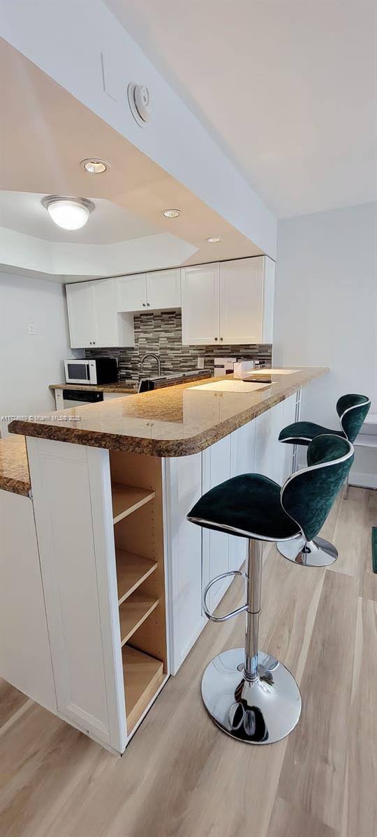 kitchen with light stone counters, light hardwood / wood-style flooring, decorative backsplash, white cabinets, and a kitchen breakfast bar