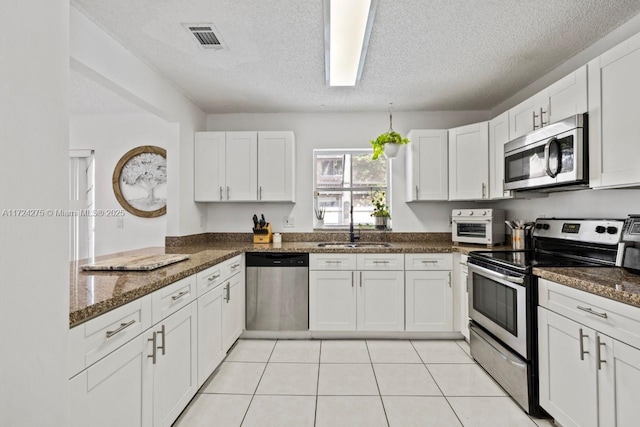 kitchen with stainless steel appliances, sink, white cabinetry, a textured ceiling, and dark stone countertops