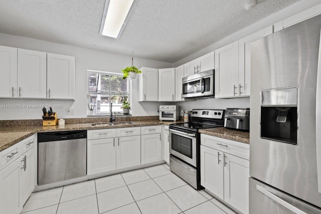 kitchen featuring sink, white cabinets, a textured ceiling, dark stone counters, and appliances with stainless steel finishes