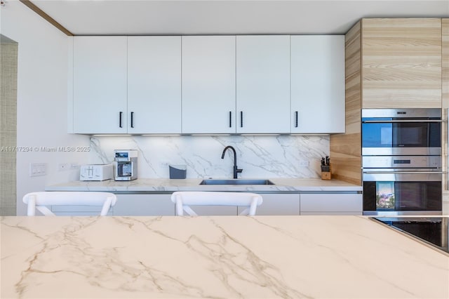 kitchen with sink, white cabinets, stainless steel double oven, and tasteful backsplash