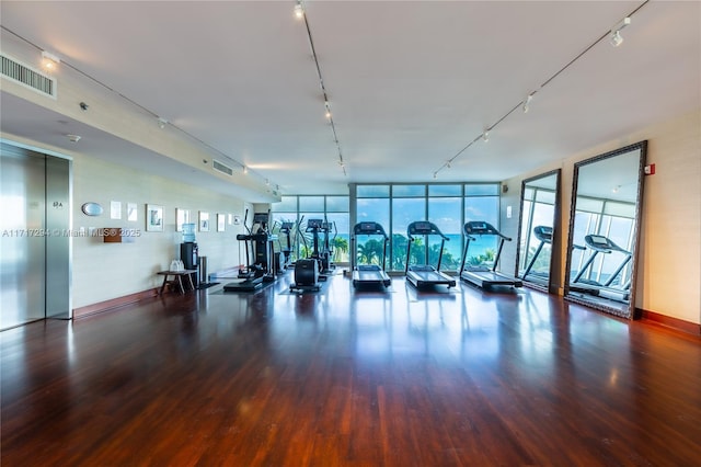 workout area featuring track lighting, a wall of windows, elevator, and dark wood-type flooring