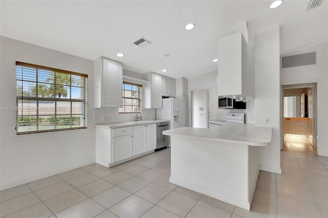 kitchen featuring appliances with stainless steel finishes, lofted ceiling, white cabinetry, kitchen peninsula, and light tile patterned floors