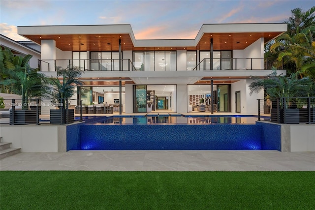 back house at dusk with pool water feature, a balcony, and a patio area