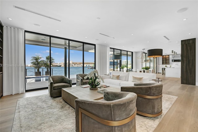 living room featuring a water view, light wood-type flooring, and a wall of windows