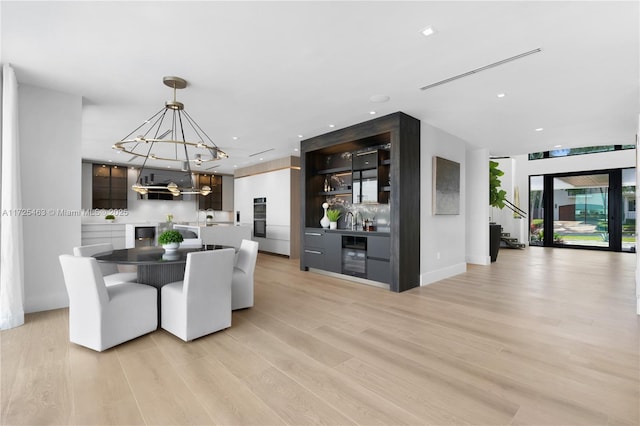 dining room with beverage cooler, a chandelier, and light wood-type flooring