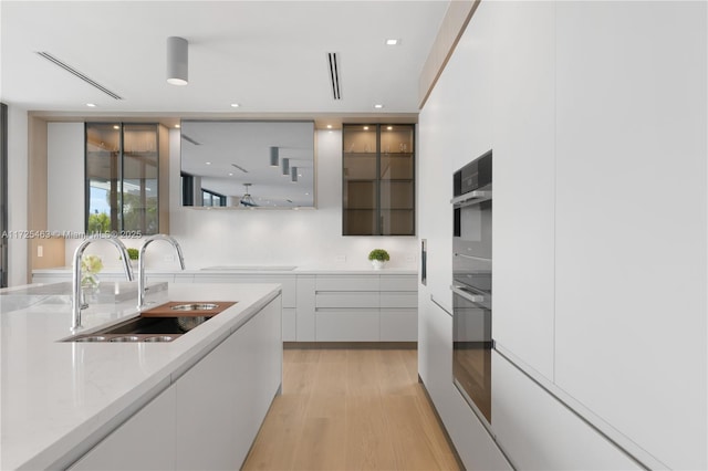 kitchen featuring white cabinetry, light stone countertops, sink, and light hardwood / wood-style flooring