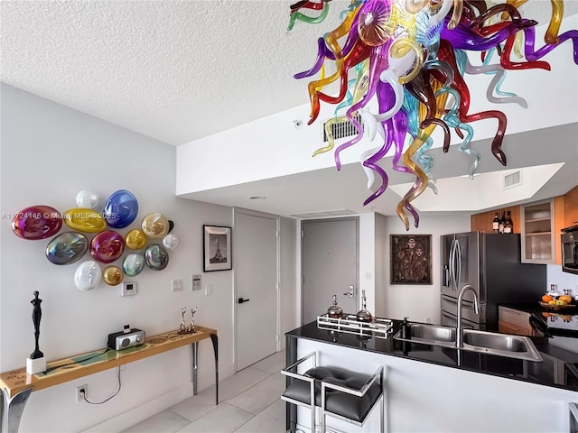 kitchen with a textured ceiling, sink, stainless steel gas cooktop, light tile patterned flooring, and fridge with ice dispenser