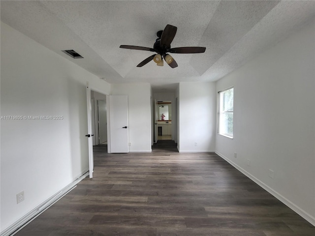 empty room with ceiling fan, dark wood-type flooring, a textured ceiling, and a tray ceiling